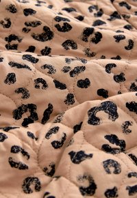 Pikowany koc z miękkiego, teksturowanego materiału w jasnobeżowym kolorze z kontrastującym, czarnym wzorem zwierzęcym.