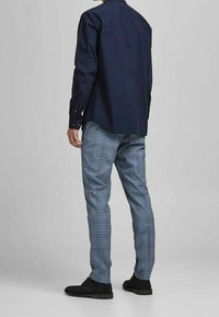 Camicia a maniche lunghe blu marina con polsini abbottonati abbinata a pantaloni slim-fit a quadri blu e scarpe nere basse.