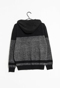 Schwarzer und grauer Kapuzenpullover mit einem Farbblockdesign, gestrickter Textur, gerippten Bündchen und einer Aufhängeschlaufe an einem schwarzen Haken.