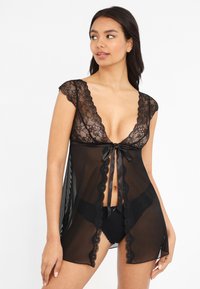 Ropa tipo kimono negro de encaje con mangas cortas, escote en V profundo y cierre de cinta de satén. Tela transparente con bordes festoneados y slit laterales.