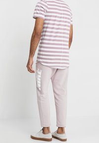 Striped short-sleeve shirt in light pink and white; paired with pink sweatpants featuring a large white logo on the side; casual footwear.