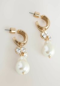 Goldene Creolenohrringe mit klaren Kristallen und einem großen Perlenanhänger. Glatte metallische Oberfläche mit glanzvollem Finish und tropfenförmigem Design.