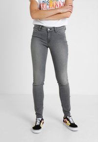 Jeans skinny grises hechos de denim con un acabado desgastado. Presentan un diseño clásico de cinco bolsillos y un cierre de botón. Combinados con zapatillas coloridas.