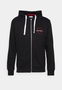 Sudadera negra con cremalleras y cordones blancos, bolsillo canguro y logo circular rojo en el lado izquierdo del pecho que dice "Jack & Jones."