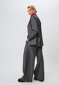 Harmaa raitapuku, jossa on rakenteellinen bleiseri ja leveälahkeiset housut. Bleiserin alla on tekstuurinen vaaleanpunainen asuste.