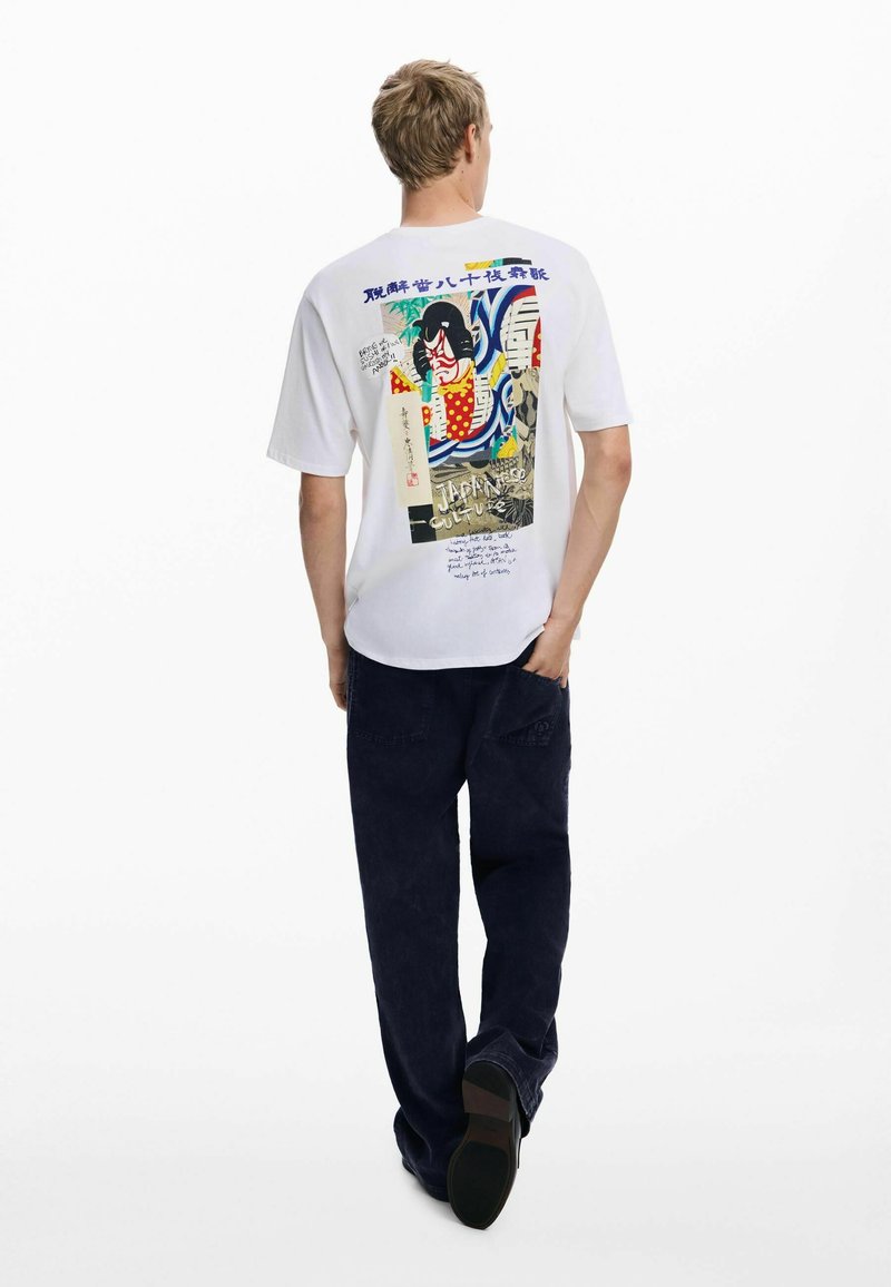 Valge T-särk, mille seljal on graafiline print, mis sisaldab Jaapani kultuuri elemente, kombineeritud tumesiniste pükste ja mustade jalanõudega.