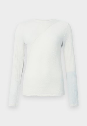 White long-sleeve top with textured fabric, featuring a diagonal seam and a light blue accent on the lower sleeve, round neckline.