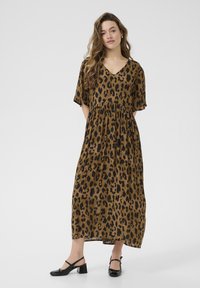 Robe maxi en tissu marron avec imprimé léopard noir, présentant un décolleté en V, des manches courtes et une taille froncée. Associée à des chaussures à talons noires.