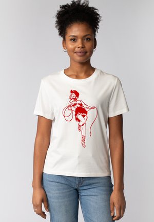 T-shirt en coton blanc avec une illustration graphique rouge d'une personne portant un chapeau de cowboy, un lasso, une jupe courte et des bottes de cowboy.