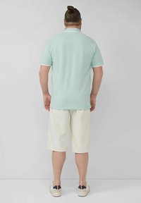 Mintgrünes Poloshirt mit weißen Streifen am Kragen und an den Ärmeln, kombiniert mit weißen knielangen Shorts und weißen Sneakers.