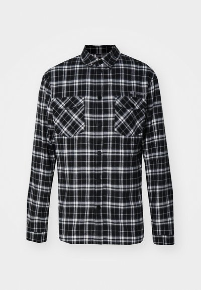 Camisa de franela a cuadros en blanco y negro con un diseño de botones, mangas largas, dos bolsillos frontales y un sutil detalle de costura.