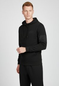 Svart zip-up hoodie i mjukt och stretchigt material. Har en huva, sidofickor och en enfärgad logotyp på bröstet och ärmarna.