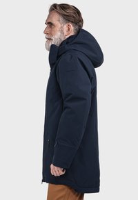 Marineblauer wasserdichter Mantel mit Kapuze, ausgestattet mit einem Reißverschluss vorne, Seitentaschen und einer glatten Textur. Verstellbare Manschetten und Saum.