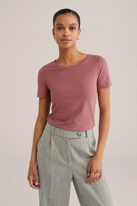 Vaaleanpunainen lyhythihainen t-paita pyöreällä kaula-aukolla, yhdistettynä harmaisiin houndstooth-kuosisin housuihin, joissa on napin yksityiskohta. Silkkinen kangas.