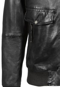 Chaqueta de cuero negra con cierre de cremallera y un bolsillo lateral, con puños y cintura de punto acanalado, que presenta una textura suave y un diseño minimalista.