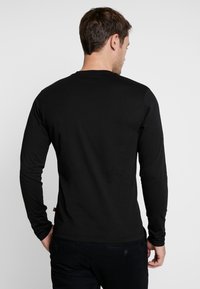 Schwarzes Langarmshirt aus Baumwolle mit Rundhalsausschnitt. Verfügt über eine glatte Textur, Slim-Fit und ein dezentes Markenzeichen nahe dem Saum.