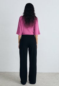 Överdimensionerad rosa topp med korta ärmar, i kombination med högmidjade svarta vida byxor. Mjuk textur, minimalistisk design och inga synliga mönster.