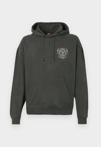 Sötétszürke kapucnis pulóver elülső zsebbel, húzózsinórral és a bal mellen egy kis fehér emblémával, amely címer és szöveg látható.