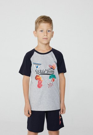 Graues und marinefarbenes T-Shirt mit kurzen Ärmeln und bunten Druckmotiven, darunter der Text "Wild Team" und Sportsymbole, kombiniert mit dunklen Shorts.