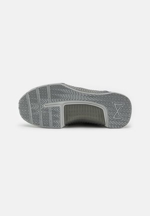 Semelle de sneaker grise avec une surface texturée, présentant des rainures de traction distinctes et un motif circulaire près du talon.