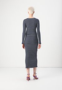 Μη επανειλημμένο φόρεμα midi σε σκούρο μπλε και λευκές ρίγες, εφαρμοστό σχήμα, ραβδωτή υφή, συμπληρωμένο με μωβ ψηλοτάκουνα πέδιλα.