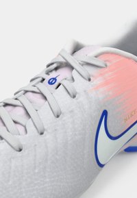 Κοντινή λήψη ενός λευκού και ροζ παπουτσιού Nike με γκρίζες κορδόνες και ένα λευκό λογότυπο swoosh με μπλε περίγραμμα.