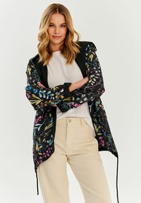 Ľahká čierna bunda s kvetinovým vzorom, dlhými rukávmi, sťahovacím spodným okrajom a kontrastným golierom. V štýle s béžovými nohavicami.
