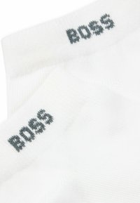 Fehér pamut zoknik bordás mintával és szürke "BOSS" logóval a felső részen. Egyszerű dizájn, amely alkalmas hétköznapi viseletre.