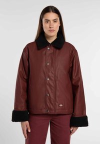 Bordeaux faux leren jack met zwarte schapenvacht kraag en manchetten, voorzien van een drukknoopsluiting en zijzakken. Subtiel logo op de zoom.