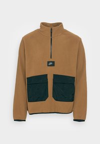 Brun fleece-pullover med hög krage, delvis dragkedja och svarta nylonfickor. Har en Nike-logotyp på bröstet.