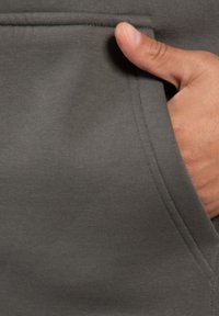 Sudadera de color gris oscuro con un bolsillo lateral, tejido acanalado y una mano apoyada en el bolsillo, mostrando la suave textura del material.