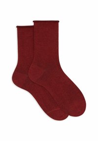 Un paio di calzini a crew di un rosso scuro semplice, distesi su uno sfondo bianco.