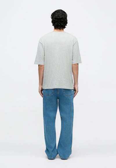 Graues T-Shirt mit kurzen Ärmeln und lockerem Schnitt, kombiniert mit hellblauen Jeans mit weitem Bein, die Gesäßtaschen und dezente Waschung aufweisen.