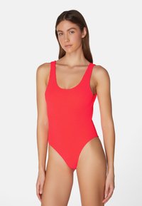 Röd randig baddräkt med rundad halsringning och breda axelremmar. Har höga benutskärningar och en mjuk textur.