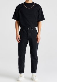 Camiseta negra de manga corta combinada con pantalones vaqueros negros de cintura alta. Destaca una cadena alrededor del cuello y zapatillas blancas. Ajuste casual.