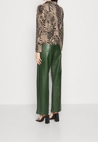 Langarm T-shirt met een beige en zwart dierenprint, gecombineerd met groen faux leren hoge taille wijde broek en zwarte blokhak sandalen.