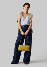 Borsa a tracolla gialla trapuntata con un motivo a diamante, completata da un top azzurro, un gilet in maglia beige e pantaloni in denim scuro a vita alta.