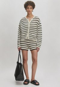 Gehaakte cardigan en shortset in zwart en crème strepen, met een knoopsluiting aan de voorkant, een casual pasvorm en een gladde textuur. Model houdt een zwarte tote.