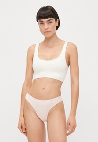 Hvit, tettsittende bralette med brede stropper og firkantet utringning, sammen med lyserøde, lavt midje truser. Glatt tekstur, minimalistisk design.