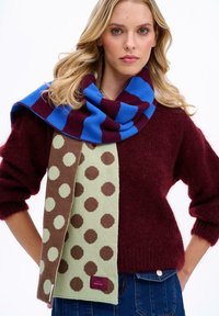 Pletený šál s modro-kaštanovým pruhovaným vzorom a zeleno-hnedým bodkovaným vzorom, vyrobený z mäkkej tkaniny.