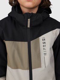 Bambino che indossa una giacca nera, beige e grigio chiaro con una zip frontale e la scritta "BRUNOTTI dal 1979" stampata sul petto.