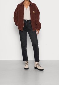 Brown corduroy jacket with a zipper, black jeans, and beige lace-up ankle boots, featured on a plain background.