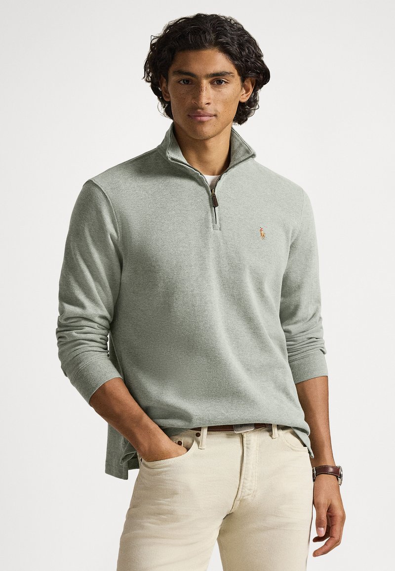 Light green, textured quarter-zip pullover with long sleeves. Features a small embroidered logo on the chest and is paired with light-colored pants.