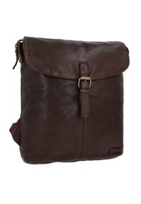 Sac à dos en cuir marron avec un rabat, doté d'une boucle en métal, d'une texture lisse et de détails de coutures visibles. Poche zippée sur le côté incluse.