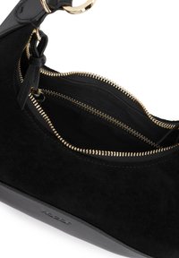 Sac à main en cuir noir et daim avec fermeture éclair dorée partiellement ouverte, montrant deux compartiments et une petite étiquette en cuir sur le curseur de la fermeture éclair.