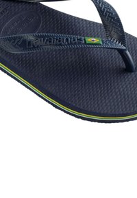 Infradito in gomma blu navy con soletta texturizzata, sottili cinturini e logo della bandiera brasiliana. Presenta una striscia di accento giallo e verde.