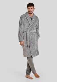 Bata de baño gris en espiga con cuello de chal y cintura ajustable, acompañada de pantalones de chándal gris claro. Tejido suave y corte relajado.