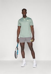 Light green polo shirt with a collar, gray shorts, and white sneakers. Holds a tennis racket, showcasing a sporty and athletic look.