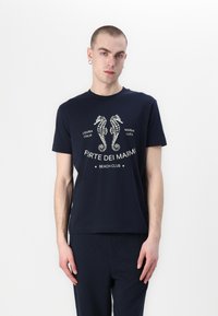 Navy zila kokvilnas T-kreklis ar divu jūras zirgānu grafiku un tekstu "Forte dei Marmi Beach Club." Īsas piedurknes un apaļa kakla dizains.