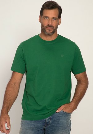 T-shirt in cotone verde con maniche corte, collo rotondo e logo discreto sul lato sinistro del petto. Indossato con jeans in denim blu. Texture liscia.